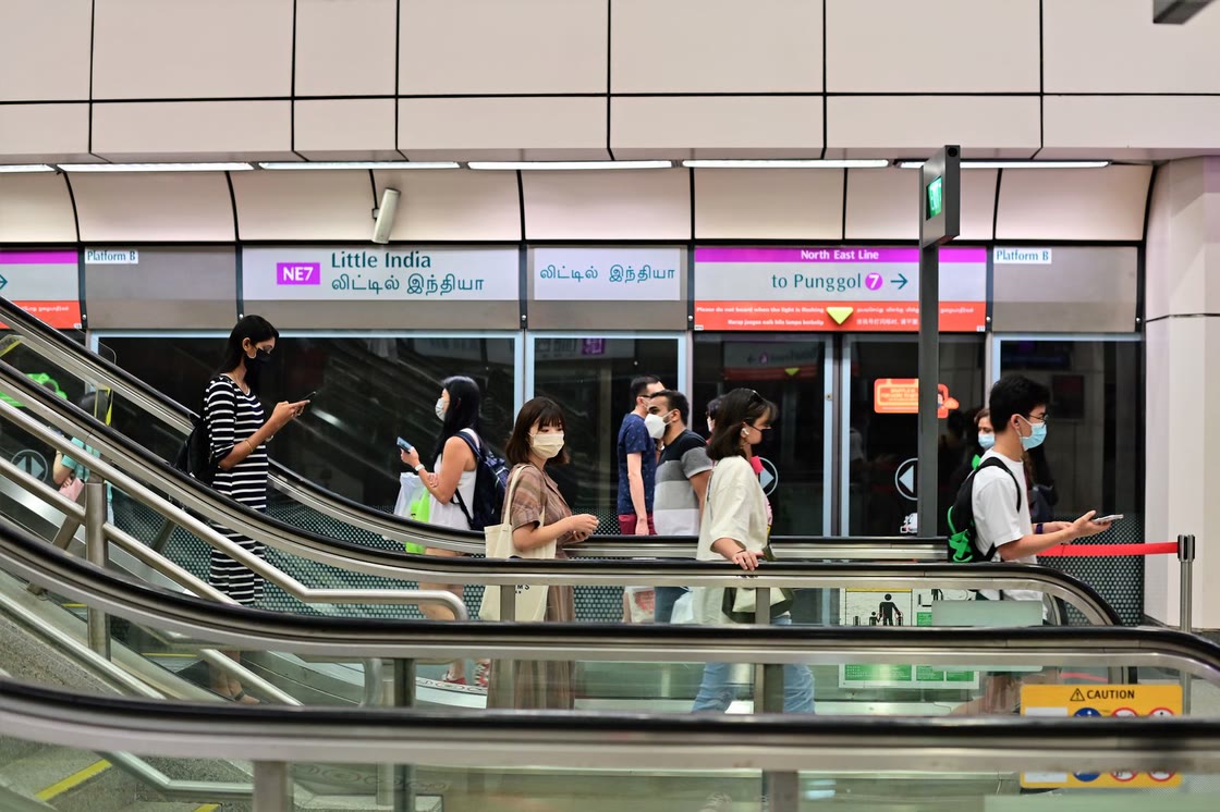 Commuters ride the escalators at Little India MRT station, under signs for the North East Line towards Punggol