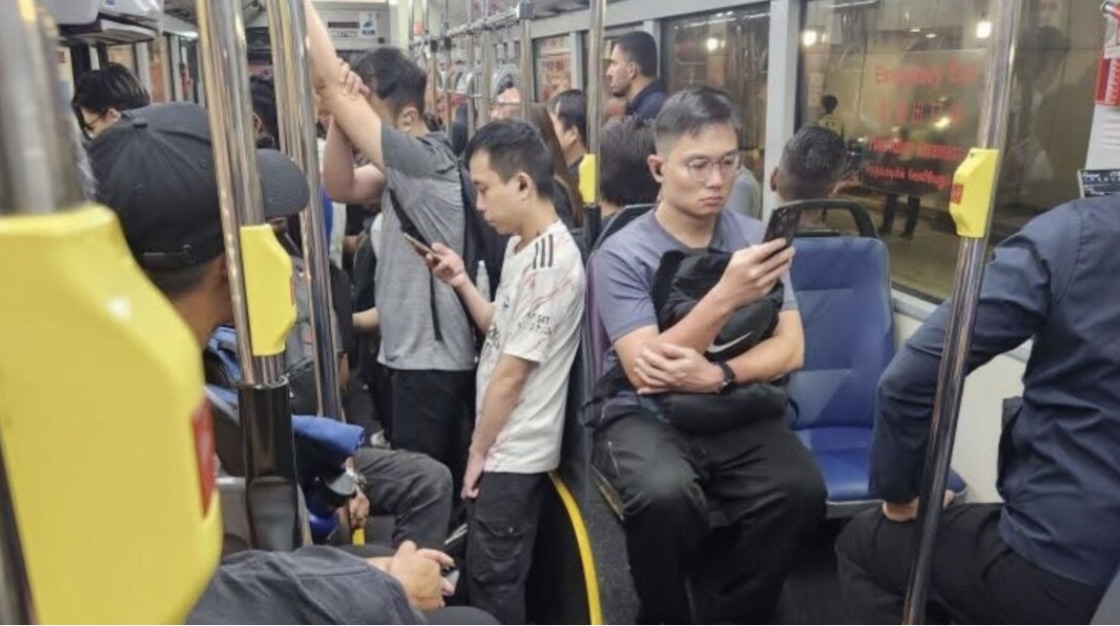 Passengers standing and sitting inside a crowded bus, several of them looking down at their phones
