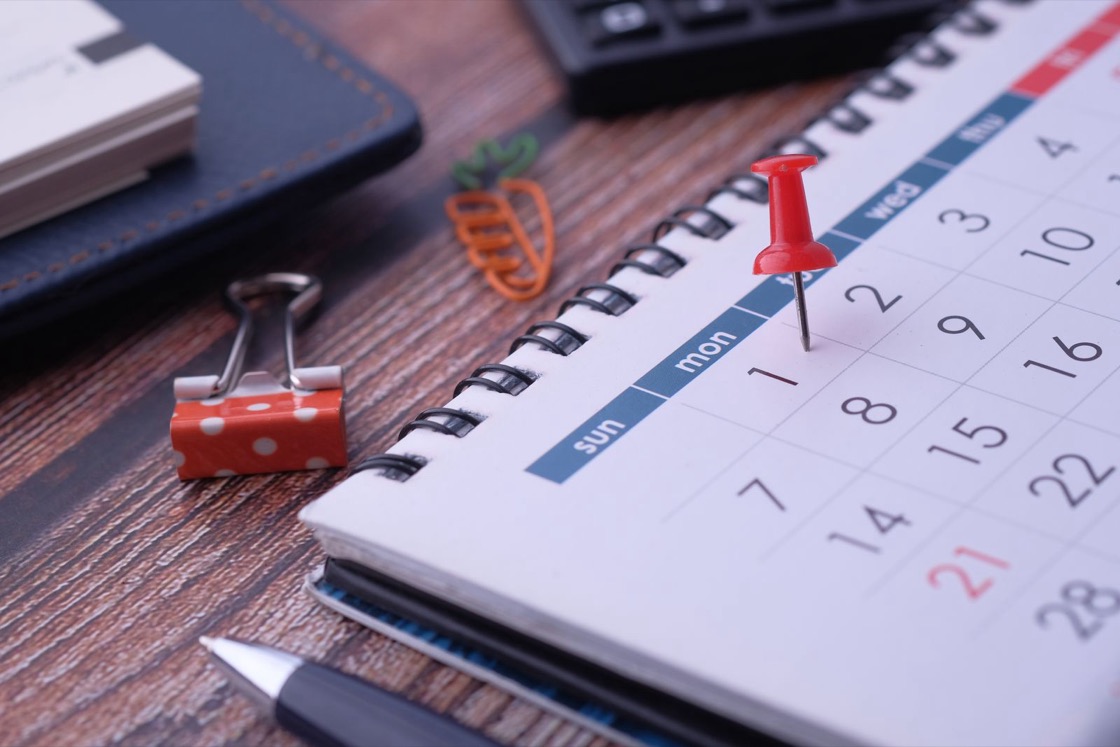A red drawing pin stuck into a date on a white desk calendar