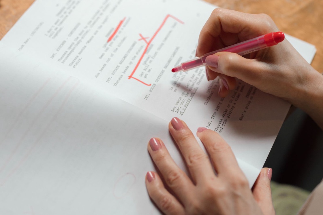 A hand holding a red pen marks corrections on a printed page