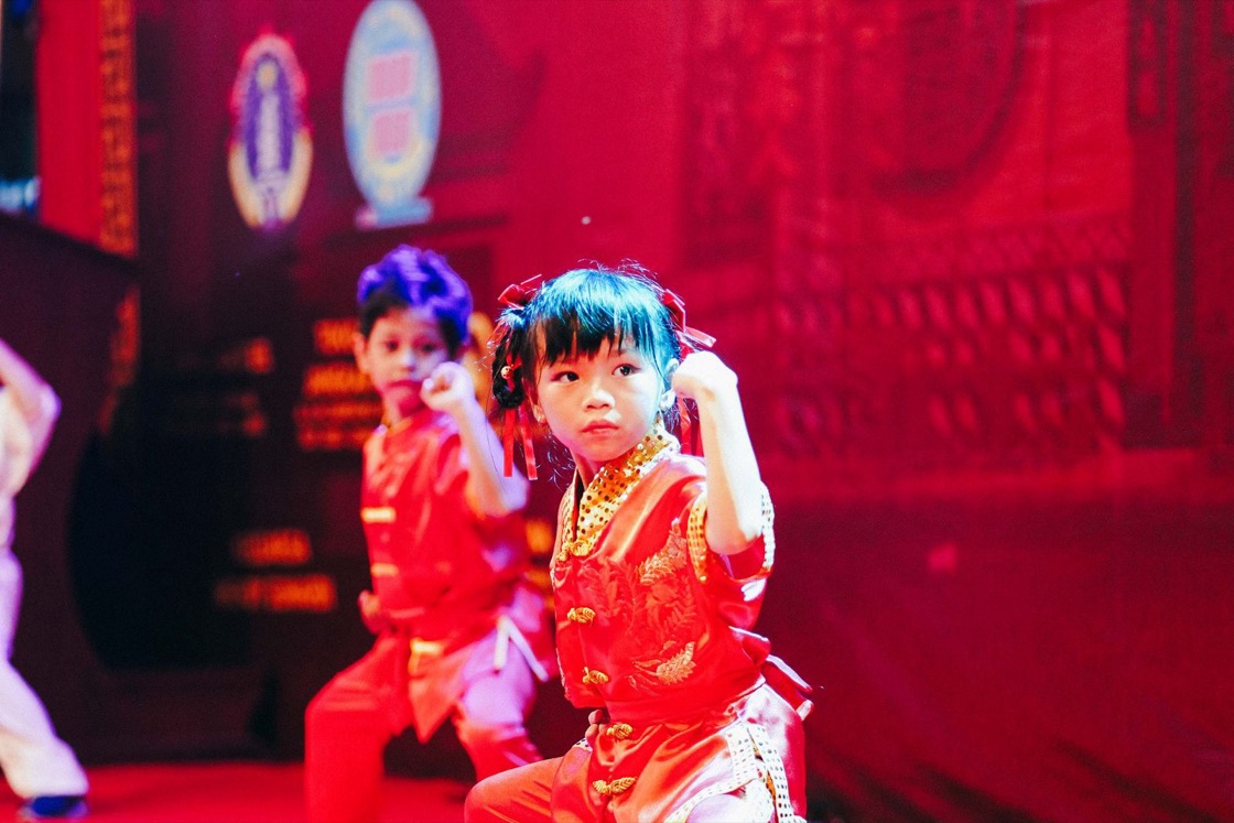 Two young children in red costumes strike confident poses on a brightly lit stage