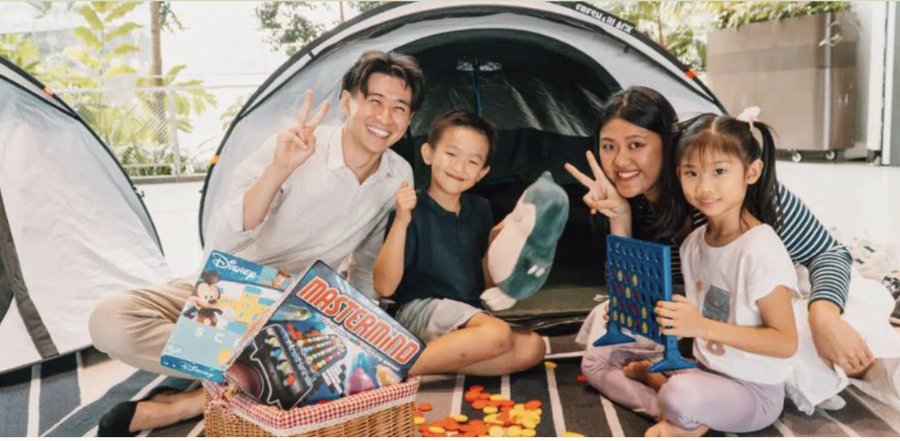A family of four smiling inside a tent, playing a board game together